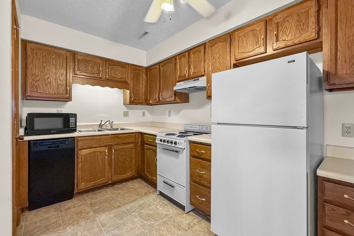 A kitchen with oak cabinets, a white refrigerator and range, a black dishwasher, and a built-in desk at the end of the counter.