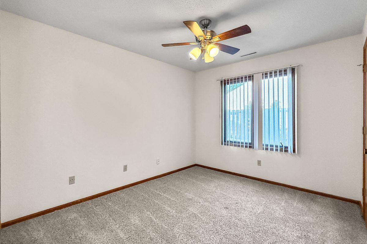 A carpeted bedroom with a ceiling fan and a window with vertical blinds.