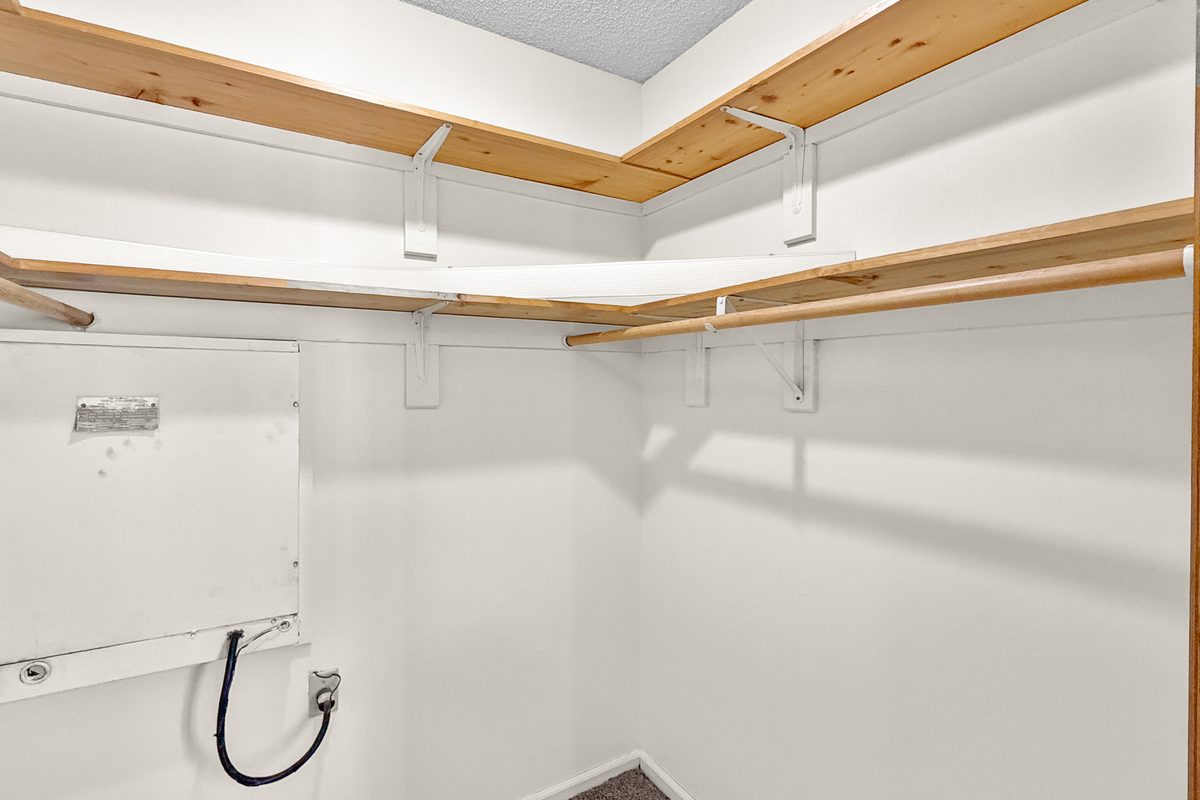 A utility room inside an apartment with three wood shelves along the wall and the water heater in the corner.