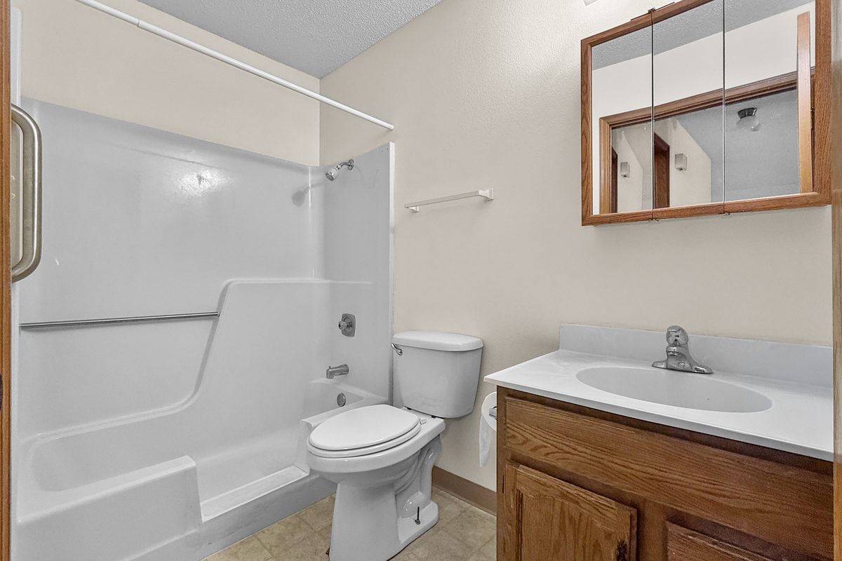 A bathroom with a tub and shower, a white toilet, an oak vanity with a white top, and a mirrored medicine cabinet.