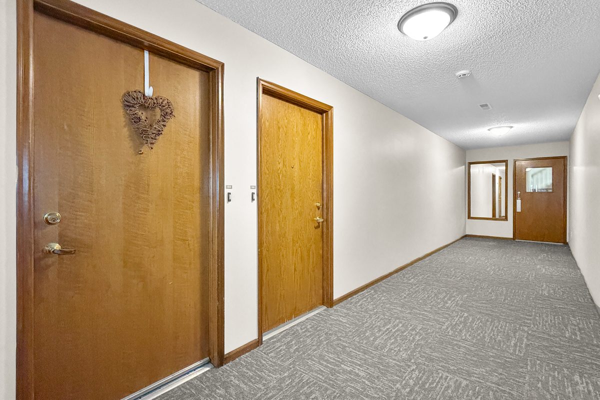 A wide carpeted hallway with apartment doors on both sides and a window at the far end.