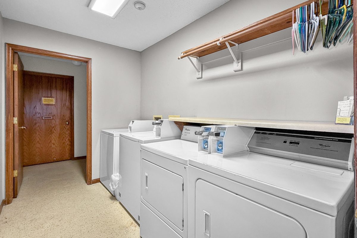A laundry room with washers and dryers along the wall and a shelf above them.