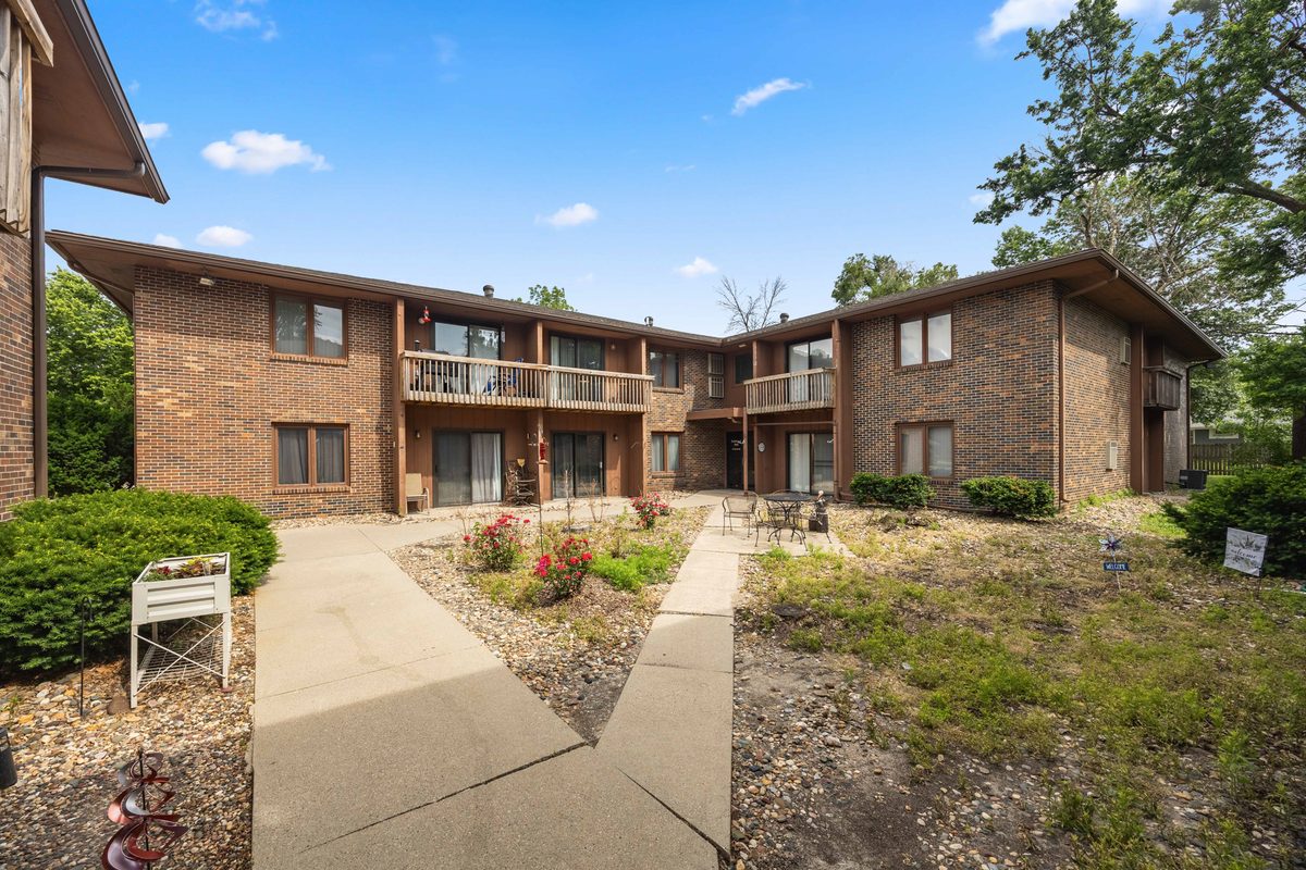 Concrete walks meeting on a lawn in front of a Trailside building, with a flower bed and a second-floor balcony above.