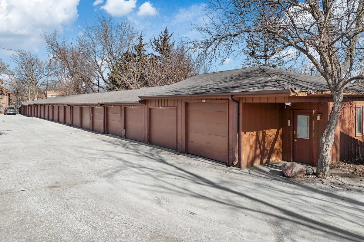 A long row of brown garage doors in one of the three garage buildings, with the paved drive in front.