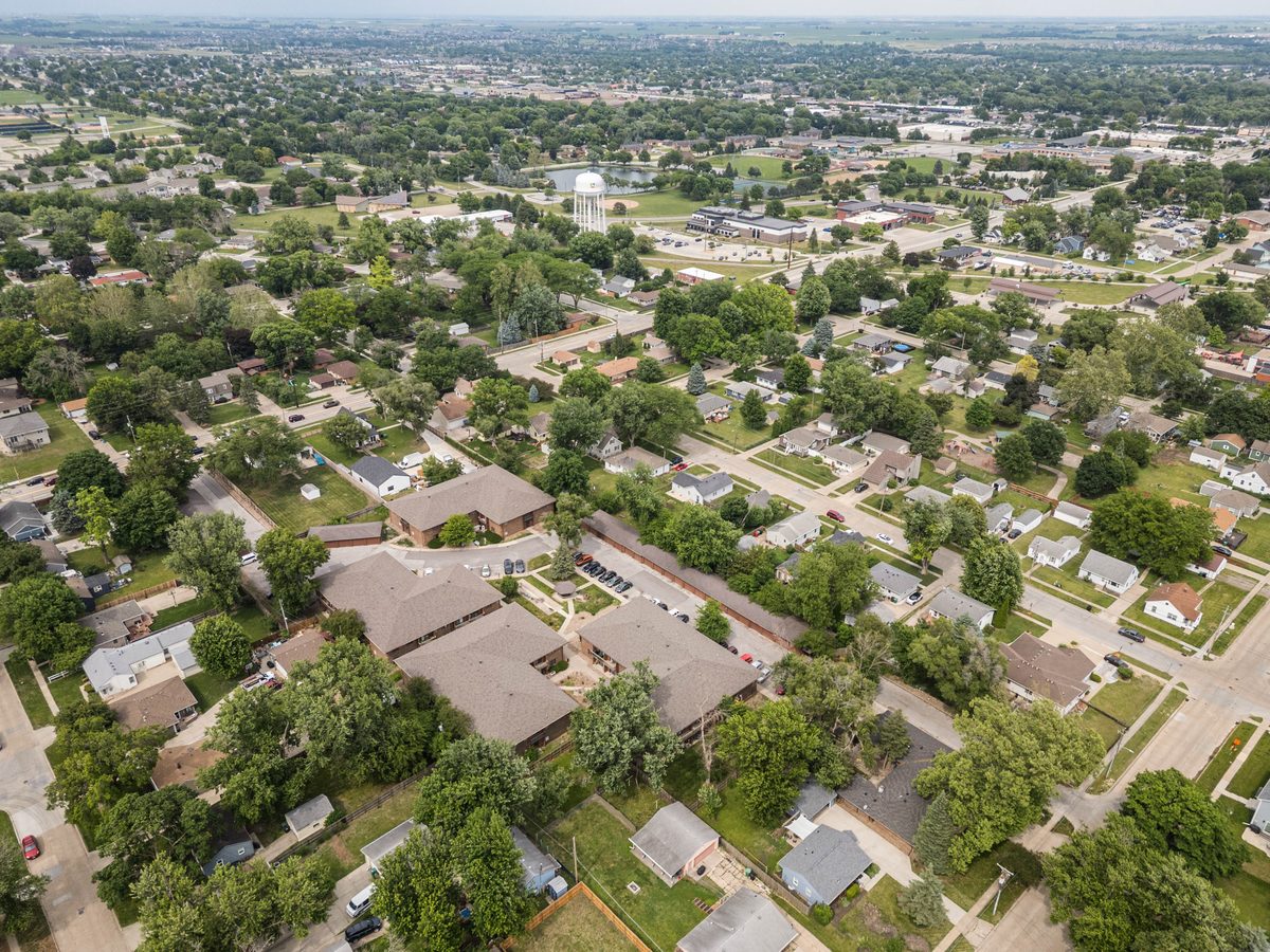Aerial view of Trailside in summer, four brick buildings with grey roofs among mature trees, with Ankeny stretching out to the horizon.